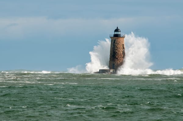 Photo of lighthouse being struck by an ocean wave